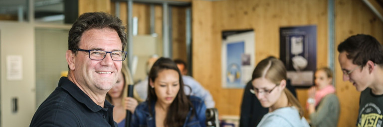 Eine Gruppe von Menschen in einem Raum, die miteinander interagieren, während ein Mann in der Mitte lächelt.