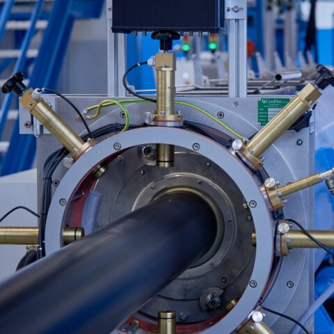 Eine industrielle Maschinenanlage mit einem langen schwarzen Rohr und mehreren Geräteteilen, im Hintergrund blaue Wände und eine Treppe.