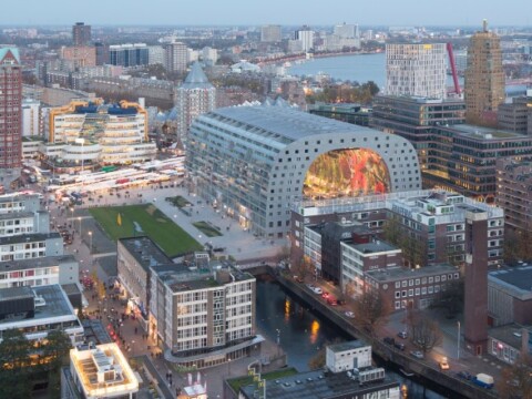 Aerial view of a modern urban area featuring a large, uniquely shaped building, shops, and a waterfront.