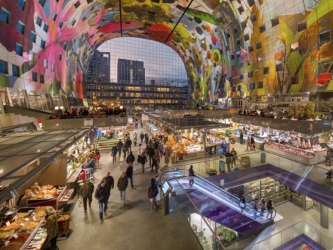 A vibrant indoor market space with colorful, large murals on the ceiling, bustling with visitors and various food stalls.