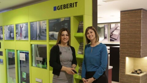 Zwei Frauen stehen vor einer farbigen Wand mit Produktpräsentationen und dem Geberit-Logo.