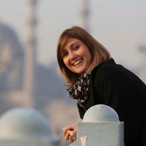 Eine lächelnde Frau in einem schwarzen Mantel lehnt an einem Geländer.