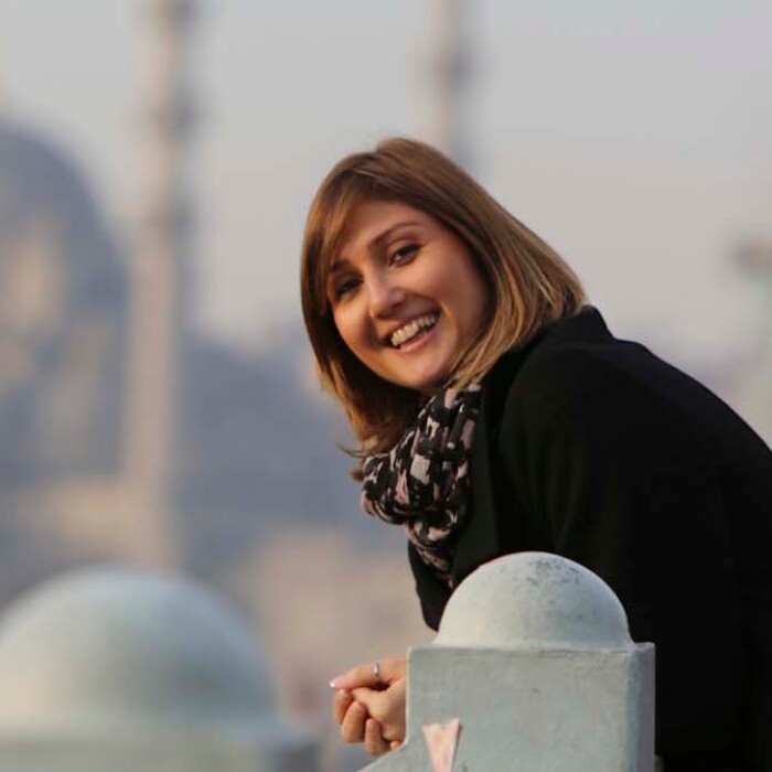 Eine lächelnde Frau in einem schwarzen Mantel lehnt an einem Geländer.