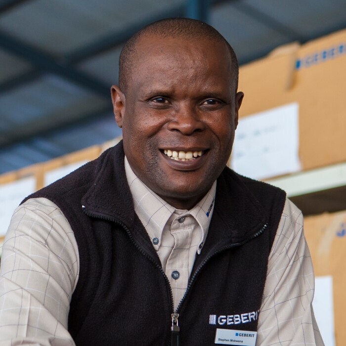 Ein lächelnder Mann in einem Lager mit Kartons im Hintergrund.