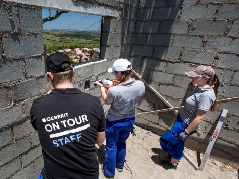 Drei Personen in Arbeitskleidung stehen an einer Baustelle und arbeiten an einer Wandöffnung in einem Rohbau.