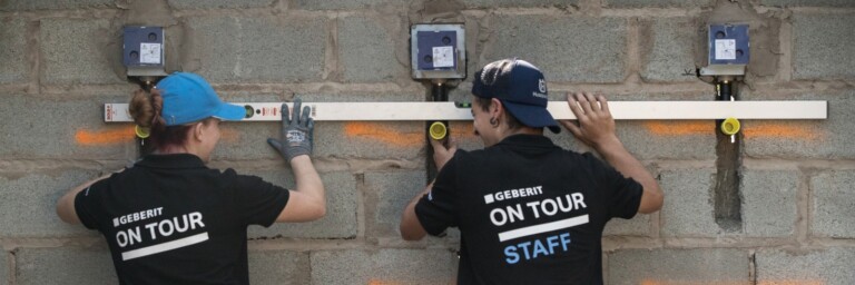 Zwei Personen in schwarzen T-Shirts arbeiten an einer Wand und benutzen eine Wasserwaage.