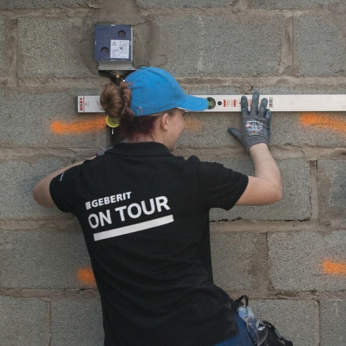 Zwei Personen in schwarzen T-Shirts arbeiten an einer Wand und benutzen eine Wasserwaage.