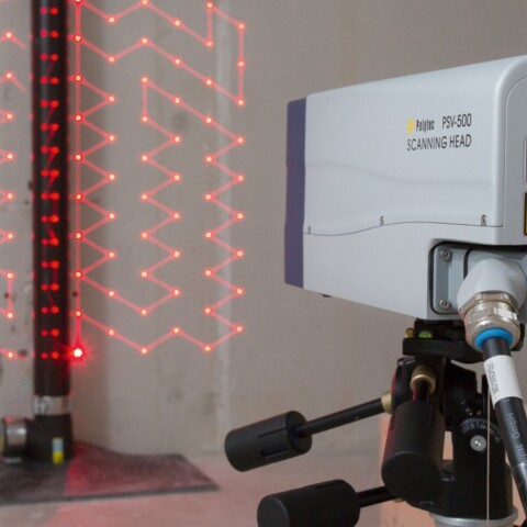 Ein Lasergerät auf einem Stativ, das rote Laserlinien an einer Wand projiziert, mit einem vertikalen Träger im Hintergrund.