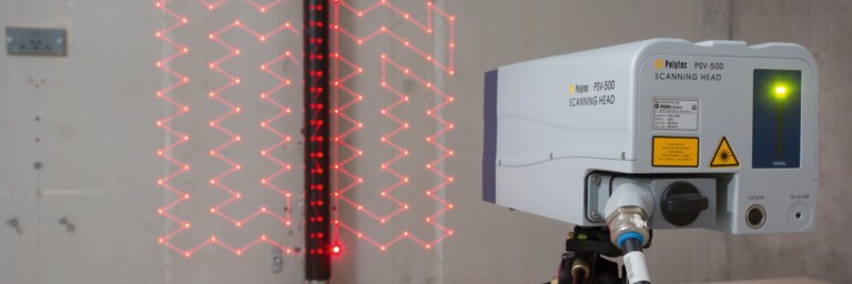 Ein Lasergerät auf einem Stativ, das rote Laserlinien an einer Wand projiziert, mit einem vertikalen Träger im Hintergrund.