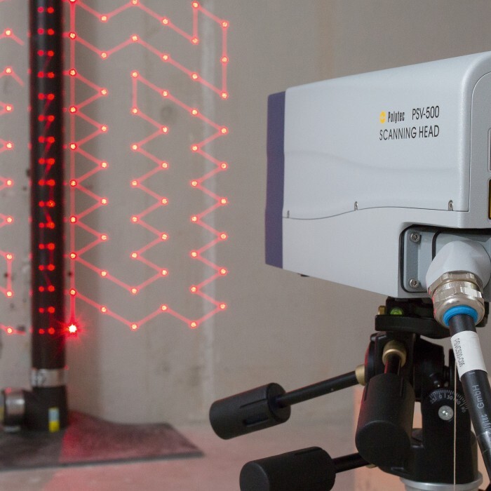 Ein Lasergerät auf einem Stativ, das rote Laserlinien an einer Wand projiziert, mit einem vertikalen Träger im Hintergrund.