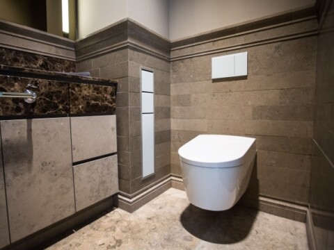 Ein modernes Badezimmer mit einer weissen Wandtoilette, edlem Steinboden und einer stilvollen Ablage aus Marmor.