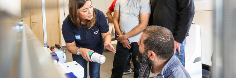 Eine Frau erklärt einer Gruppe von Männern etwas, während sie vor einer Installation stehen.