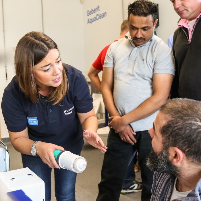 Eine Frau erklärt einer Gruppe von Männern etwas, während sie vor einer Installation stehen.