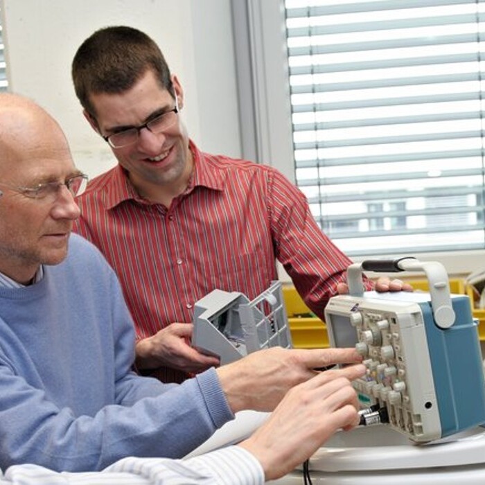 Three men are doing a test in a laboratory setting, discussing components.