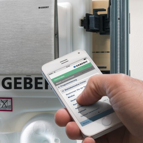 Eine Hand, die ein Smartphone hält mit einer App, um den Spülkasten zu kontrollieren.