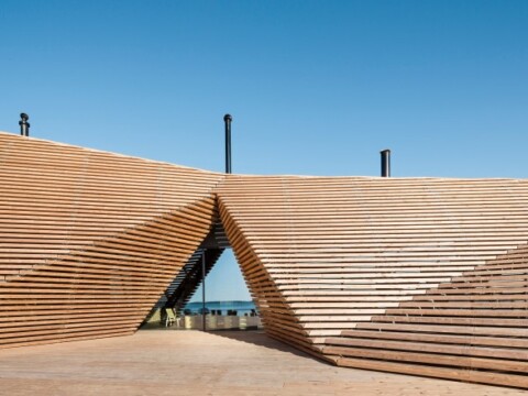 Modernes Holzgebäude mit einer dynamischen, geneigten Struktur und klaren Linien vor einem blauen Himmel.