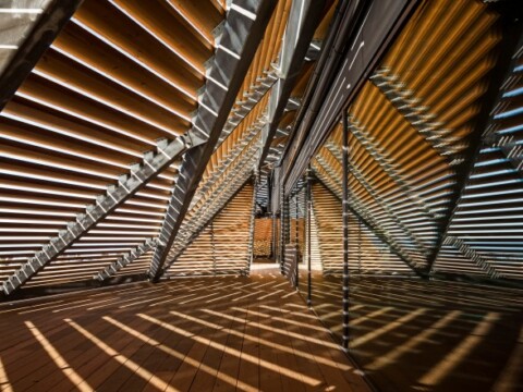 Innenansicht eines modernen Raumes mit reflektierenden Wänden und schrägen horizontalen Lamellen, die Schatten erzeugen.