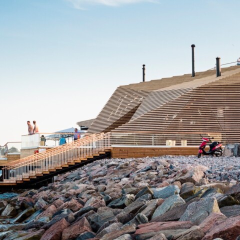 Moderne Holzarchitektur am Wasser mit Terrassen und Besuchern auf dem Dach.