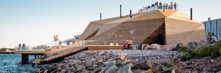 Moderne Holzarchitektur am Wasser mit Terrassen und Besuchern auf dem Dach.