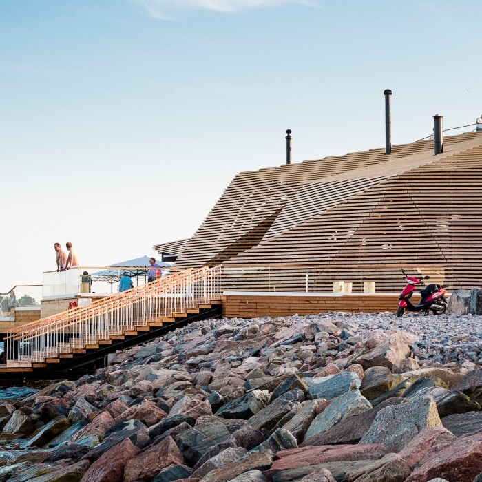 Moderne Holzarchitektur am Wasser mit Terrassen und Besuchern auf dem Dach.