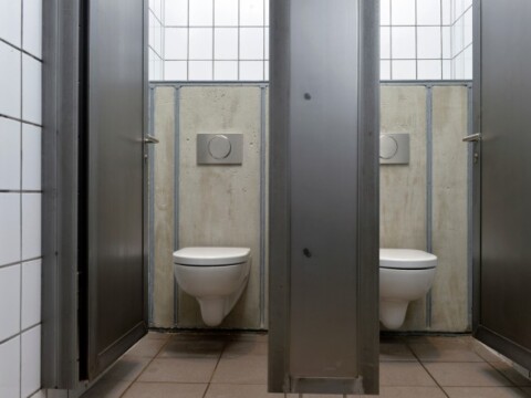 Two toilet stalls with white toilets and gray partition walls in a tiled restroom.