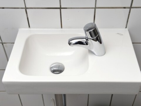 A white rectangular sink with a chrome faucet, situated against a tiled wall.