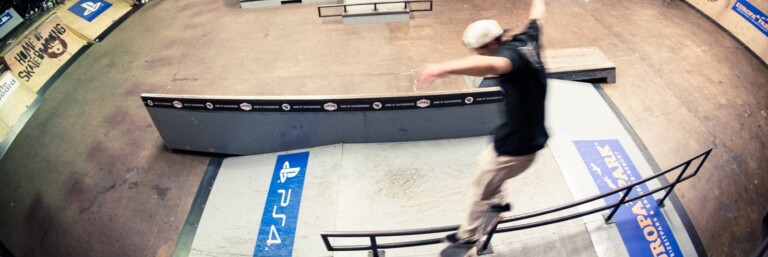 A skateboarder performing a trick on a rail in a skatepark, surrounded by spectators.
