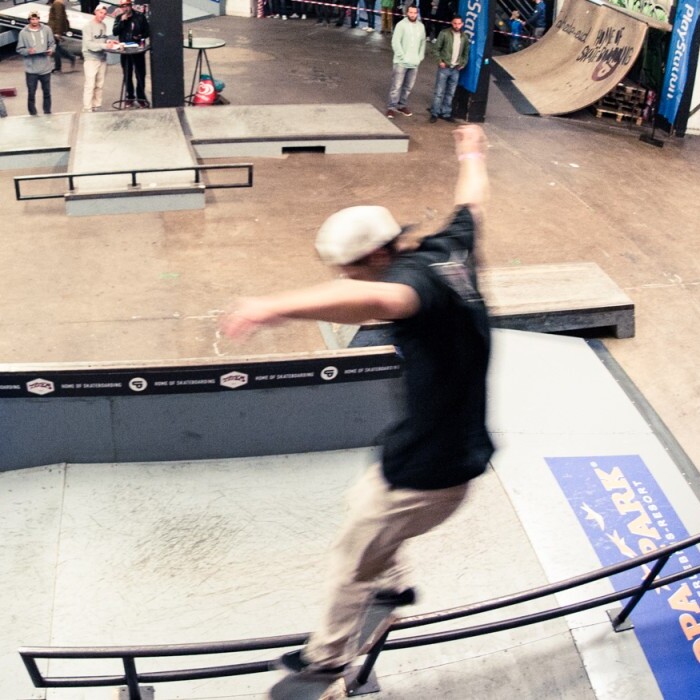 A skateboarder performing a trick on a rail in a skatepark, surrounded by spectators.