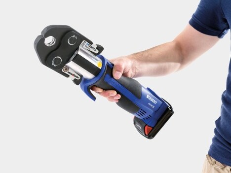 Eine Person, die ein blau-silbernes Presswerkzeug zum Pressen von Fittings und Rohren in der Hand hält.