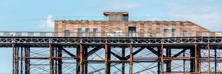 A wooden pier with a modern building on top, supported by metal pillars over a calm sea.