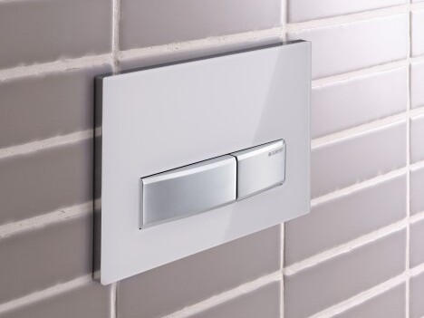 A modern dual flush toilet actuator plate mounted on a gray tiled wall.