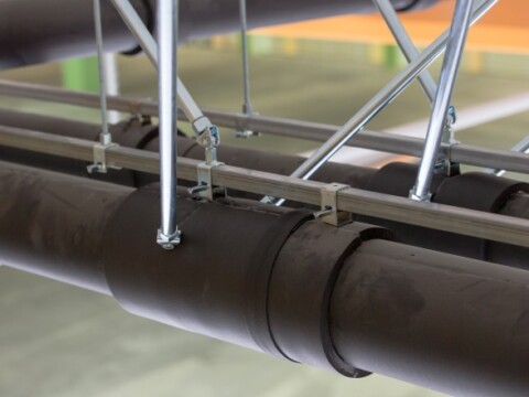 Close-up view of dark pipes secured with metal brackets and rods in an industrial setting.