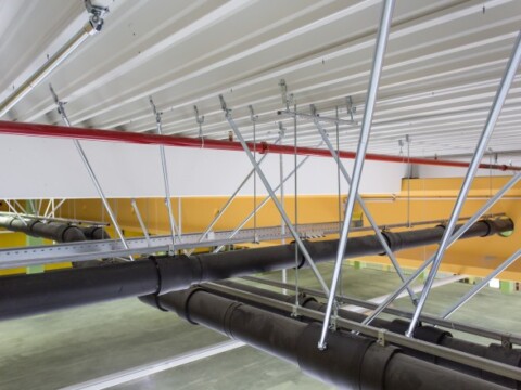 Industrial ceiling structure featuring exposed pipes and metal supports against a white and yellow backdrop.