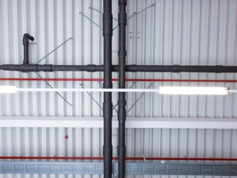 A view of a ceiling displaying black pipes and metal beams.