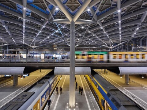 A modern train station viewed from above, showcasing multiple train tracks and platforms under a distinctive geometric roof structure.