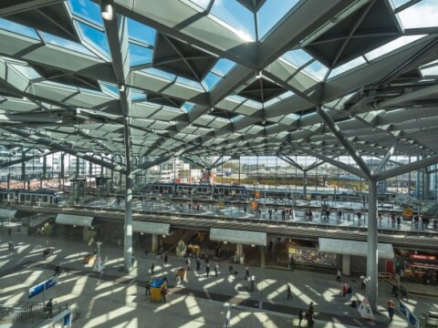 A spacious airport terminal with modern architecture, featuring a high, angular ceiling and large windows allowing natural light to enter the building.