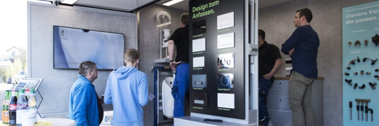 A group of people interacting with displays in a modern exhibition space featuring screens and product information.