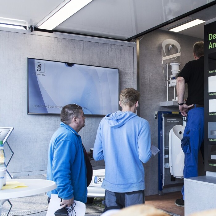 A group of people interacting with displays in a modern exhibition space featuring screens and product information.