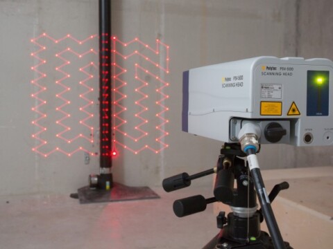 Ein Lasergerät auf einem Stativ projiziert ein rotes Rastermuster auf eine Wand.