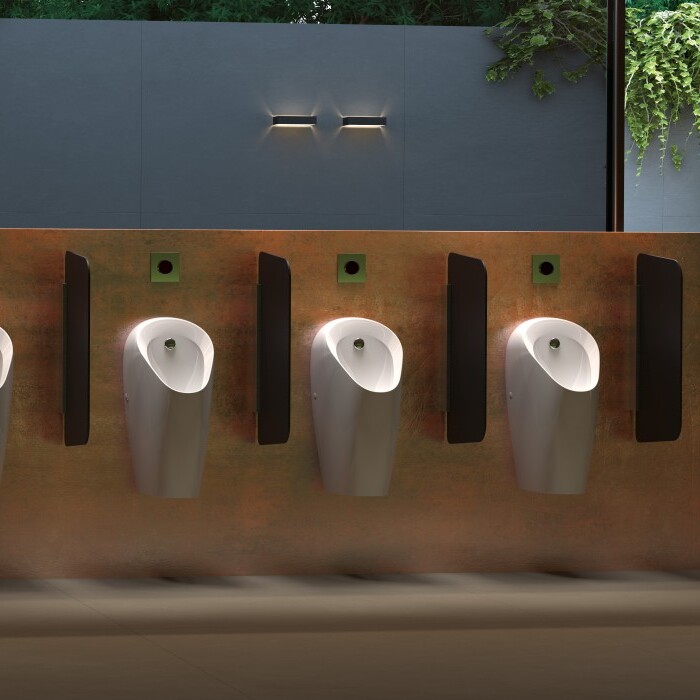 A modern bathroom interior featuring a row of four white urinals against a textured wall with greenery in the background.