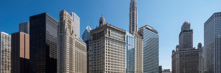 A panoramic view of a modern city skyline featuring a mix of tall skyscrapers and historic buildings under a clear blue sky.