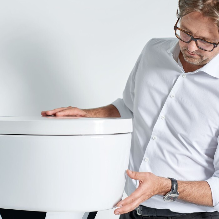 Ein Mann in einem weissen Hemd steht neben einem modernen, weissem Toilettendesign.