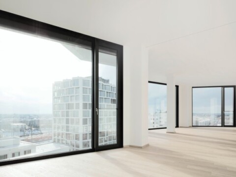 Heller, moderner Innenraum mit grossen schwarz umrahmten Fenstern und Blick auf eine Stadtlandschaft.