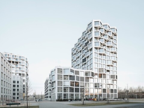 Moderne, kubische Wohngebäude mit grossen Fenstern und einzigartigen Fassadengestaltungen, umgeben von grauem Asphalt.