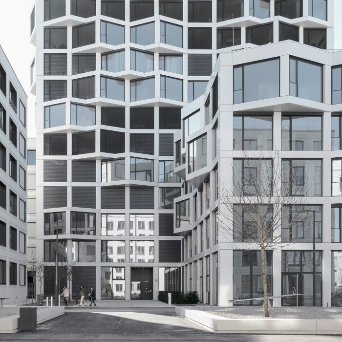 Moderne Architektur mit mehreren Gebäuden in verschiedenen Formen und Fenstergestaltungen, vor einem klaren Himmel.