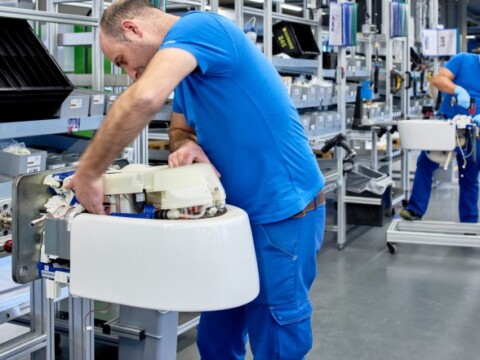 Ein Arbeiter in blauer Kleidung montiert Komponente in einer modernen Produktionshalle.