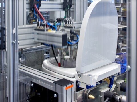 Automatisierte Maschine mit einer Toilette darin, umgeben von Metallrahmen und verschiedenen Kabeln.