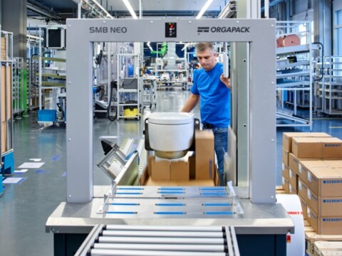 Ein Arbeiter in blauer Kleidung, der eine Verpackungsmaschine im Produktionsbereich bedient.