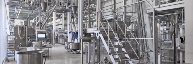 Moderne Industrieanlage mit Maschinen, Rohren und einer Treppe, die eine sterile Arbeitsumgebung zeigt.