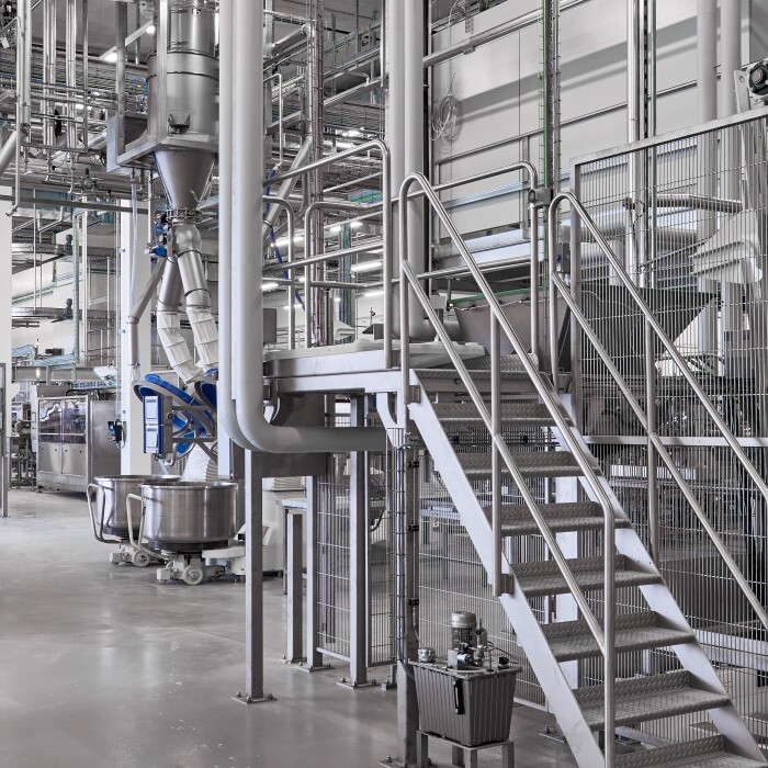 Moderne Industrieanlage mit Maschinen, Rohren und einer Treppe, die eine sterile Arbeitsumgebung zeigt.